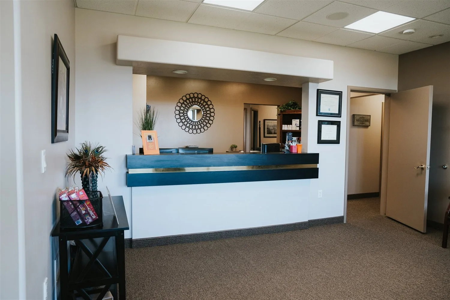 Front reception desk with dark blue trim and a decorative round mirror in a dental office lobby.